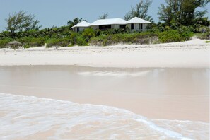 A beachfront property with a white house, sandy beach, and surrounding vegetation. - Provender 5 Bedroom Home (Savannah Sound)