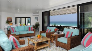 A spacious living area with wicker furniture, a glass coffee table, and a view of the ocean. - Provender 5 Bedroom Home (Savannah Sound)