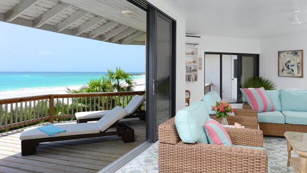A balcony with a view of the ocean, a wicker sofa with cushions, and a bookshelf. - Provender 5 Bedroom Home (Savannah Sound)
