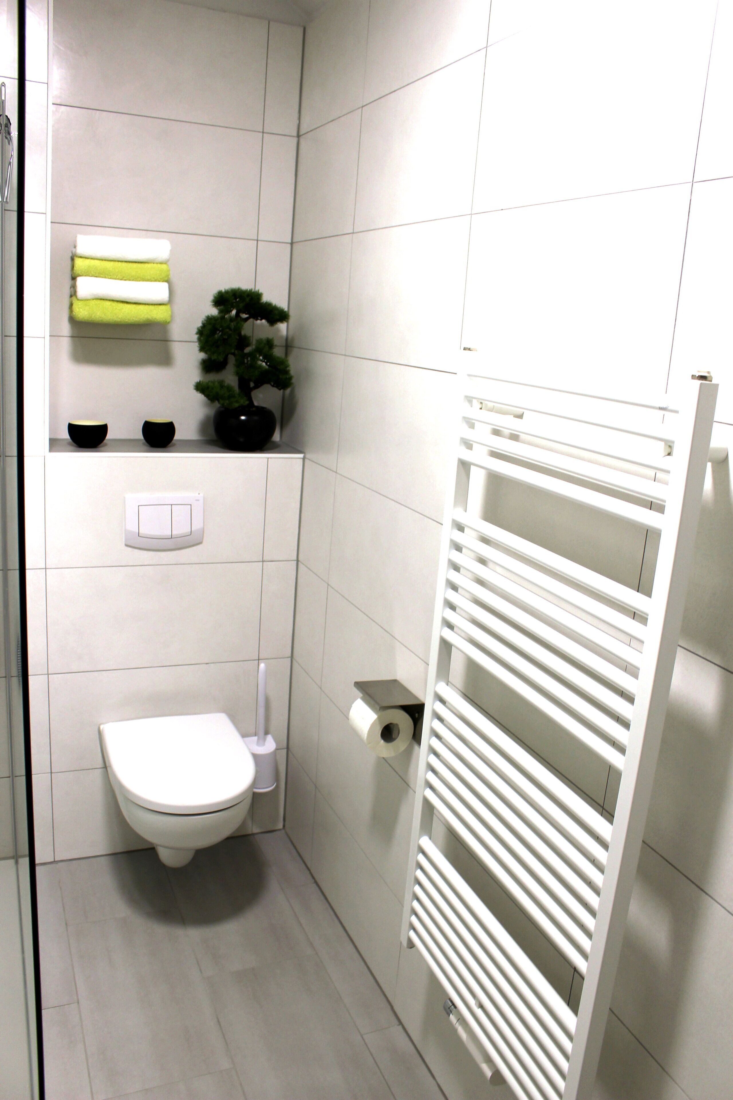 Une petite salle de bain moderne comprenant des toilettes, un porte-serviettes, un radiateur et une plante en pot.