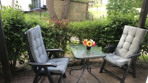 Two cushioned chairs with a glass table, a vase with flowers, and a brick patio. - Apartment Seestern Prerow/parking lot, 2 bicycles, bed linen/towels incl. (Prerow)