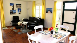 A living room with a sofa, a dining table with chairs, a lamp, and a bottle of champagne. - Apartment Seestern Prerow/parking lot, 2 bicycles, bed linen/towels incl. (Prerow)