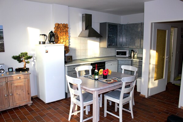 A compact kitchen with white cabinets, a microwave, and a coffee maker. There is a dining table with chairs and a small potted plant.