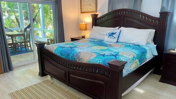 A bedroom with a large bed, a nightstand, a lamp, a window with curtains, and a view of the outdoors.