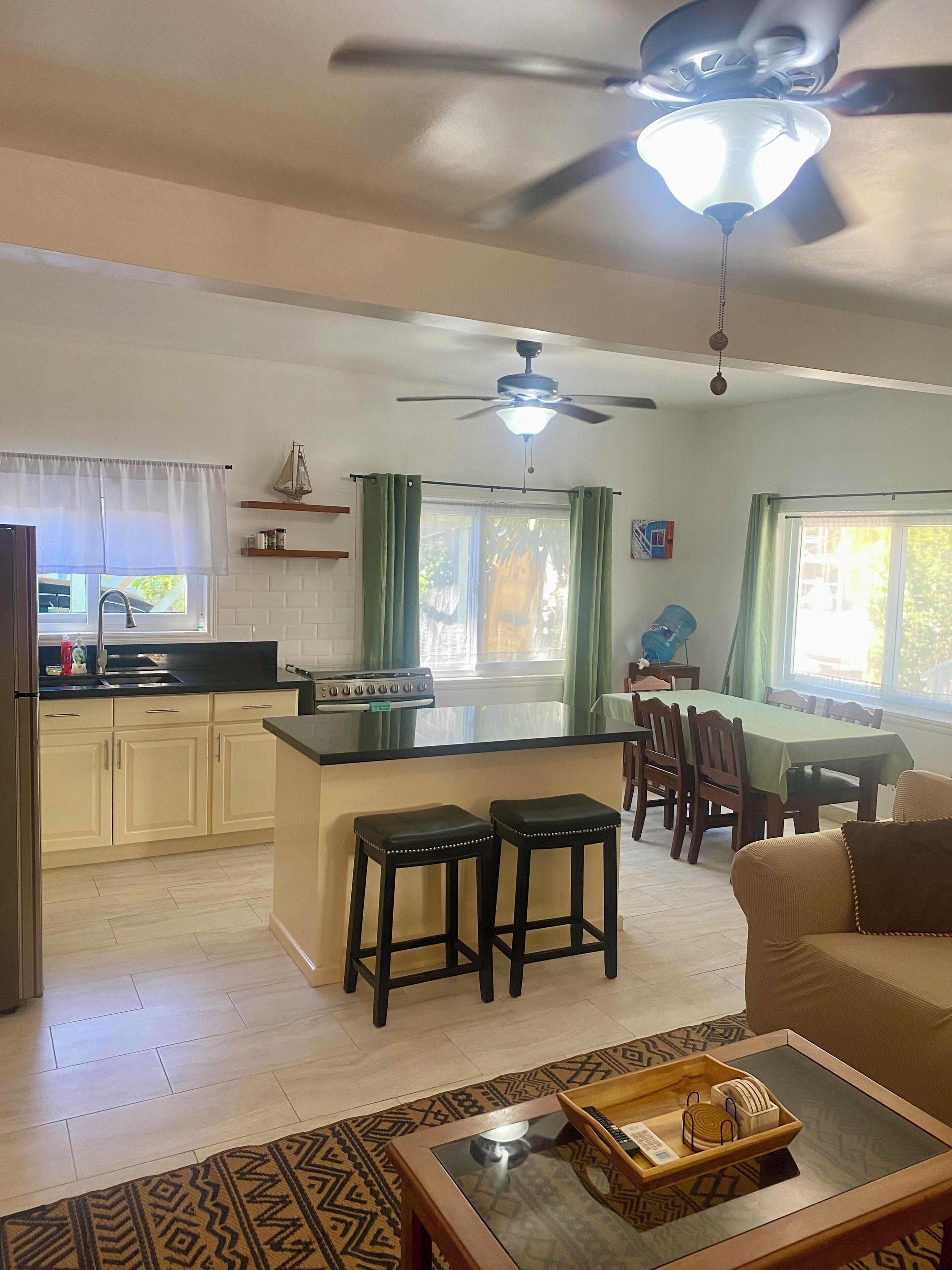 A modern kitchen with a central island, a dining area with a table and chairs, and a living room with a sofa.