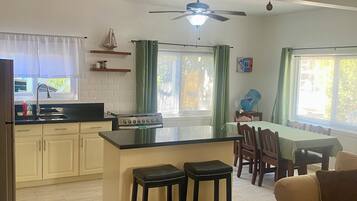 A modern kitchen with a central island, a dining area with a table and chairs, and a living room with a sofa.