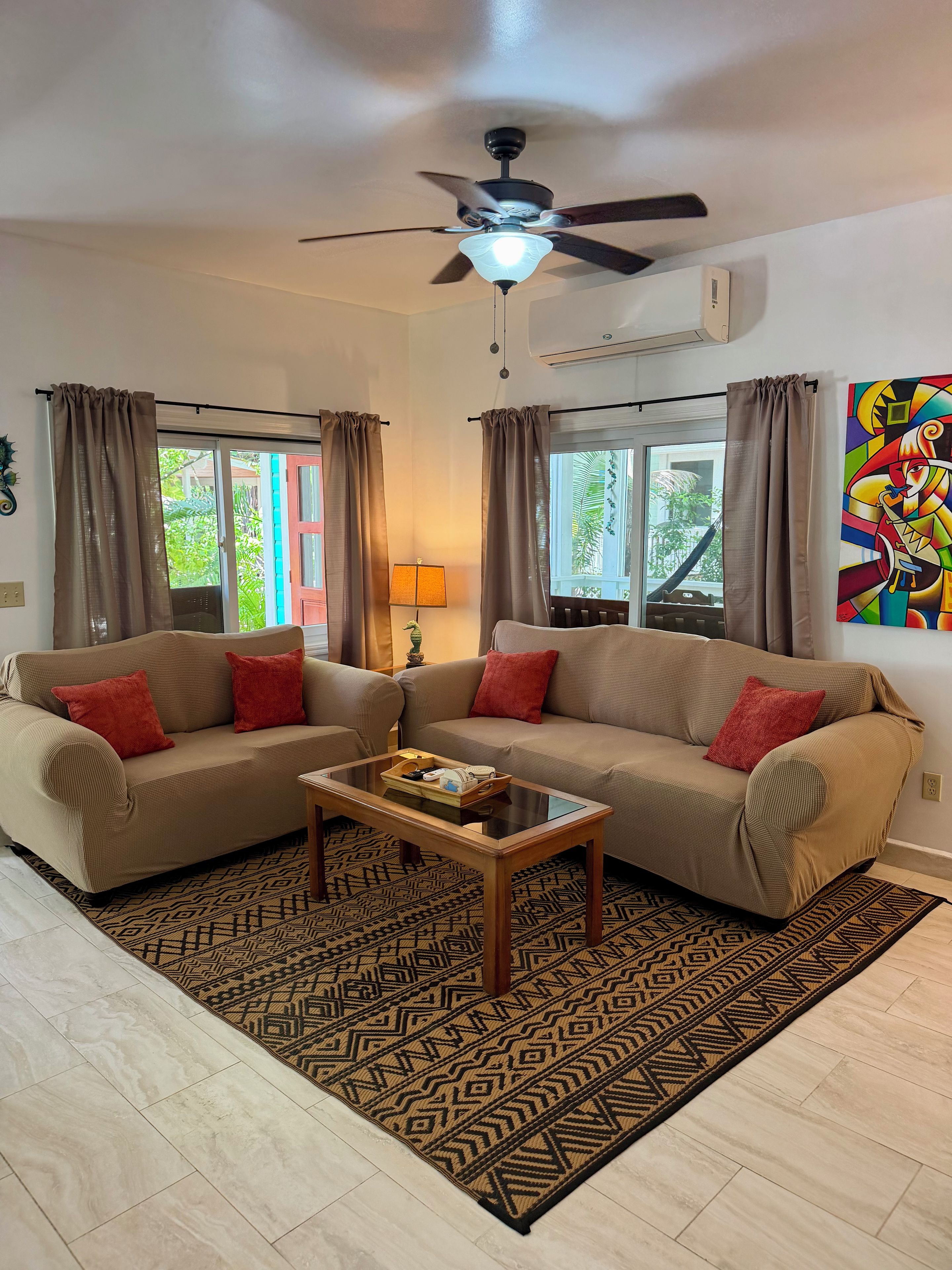A living room with a sofa, a coffee table, patterned rugs, and a ceiling fan.