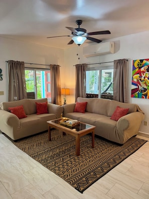 A living room with a sofa, a coffee table, patterned rugs, and a ceiling fan.
