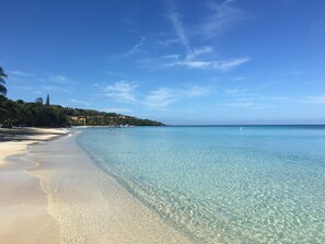 A beach with clear turquoise water, sandy shore, and a forested hillside in the background. - On the beach, equipped with backup generator (West Bay)