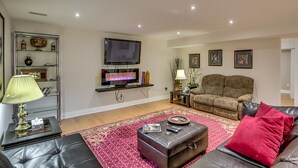 Un salon doté d’un téléviseur à écran plat, d’une cheminée, d’un canapé, d’une table basse et d’un tapis rouge à motifs.
