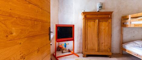 Una stanza con una porta in legno, un giocattolo rosso e blu su un piedistallo, un armadietto di legno e un letto a castello.