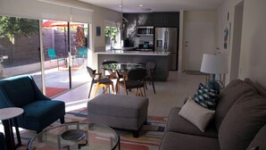 Una sala de estar moderna con una mesa de centro de vidrio, un sofá y una zona de comedor con sillas.
