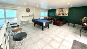 A pool table in a room with a green accent wall, a sofa, and a bar area.
