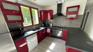 A modern kitchen with red cabinets, stainless steel appliances, and a window providing natural light.