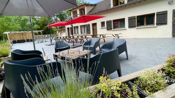 An outdoor patio area with tables and chairs, a wooden deck, and a building with windows and a balcony.