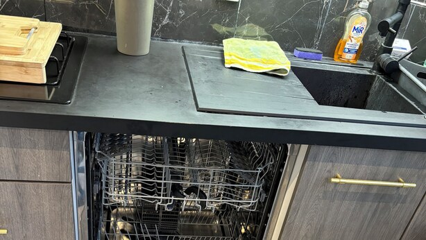 A kitchen with a built-in dishwasher, a marble backsplash, and a wooden countertop.