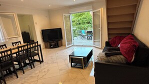 A modern living room with a dining area, a flat-screen TV, and a staircase leading to an outdoor patio.