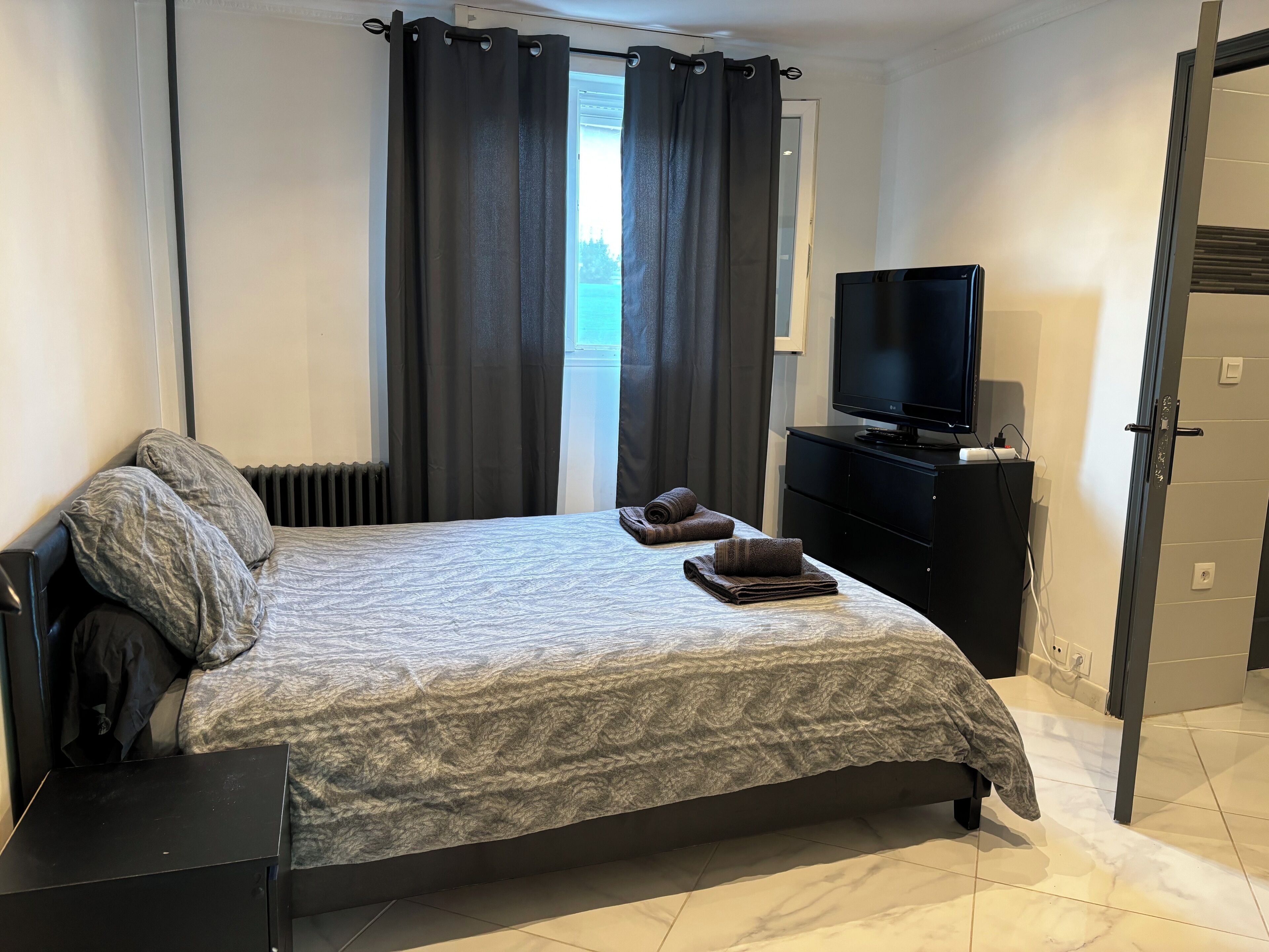 Ein Schlafzimmer mit einem Bett, einem Fernseher, einem Schminktisch und einem Fenster mit Vorhängen.