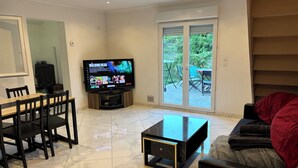 A living room with a TV, a dining table, chairs, a sofa, and a sliding glass door to a patio.
