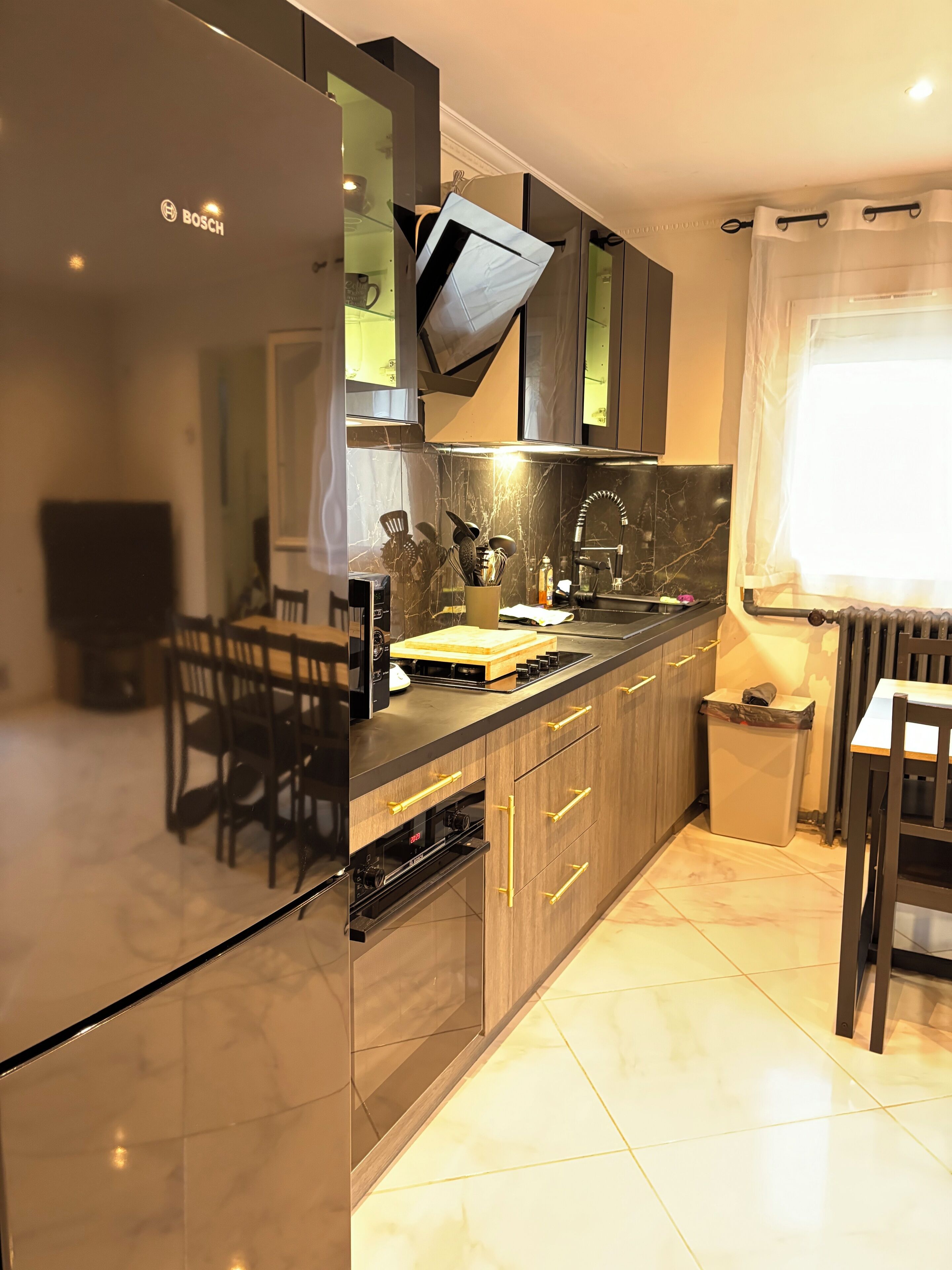 Una cucina moderna con frigorifero Bosch, mobili in legno, piano di lavoro nero e pavimento piastrellato.