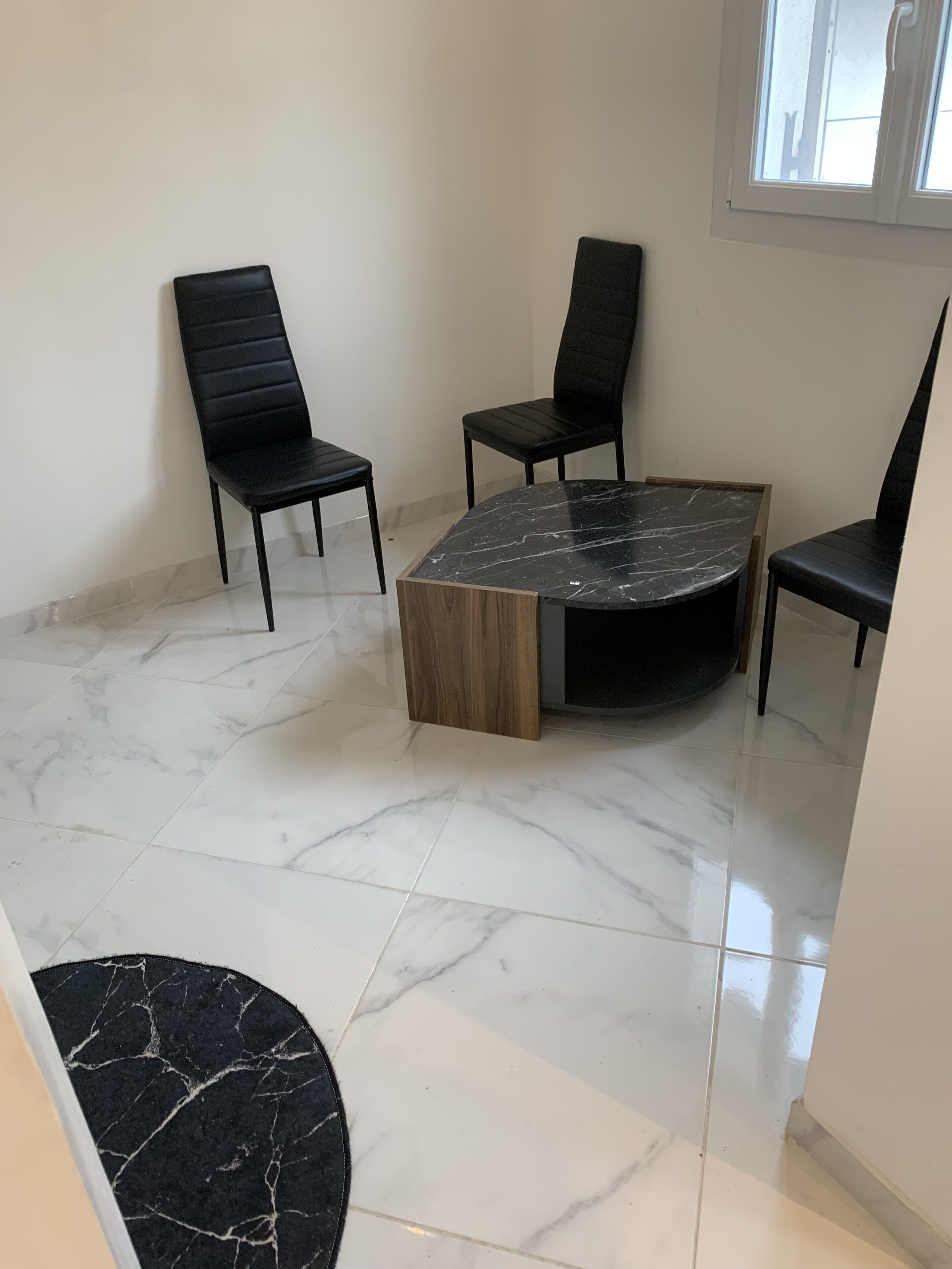 A room with a marble floor, a round table with a wooden base, and four black chairs.