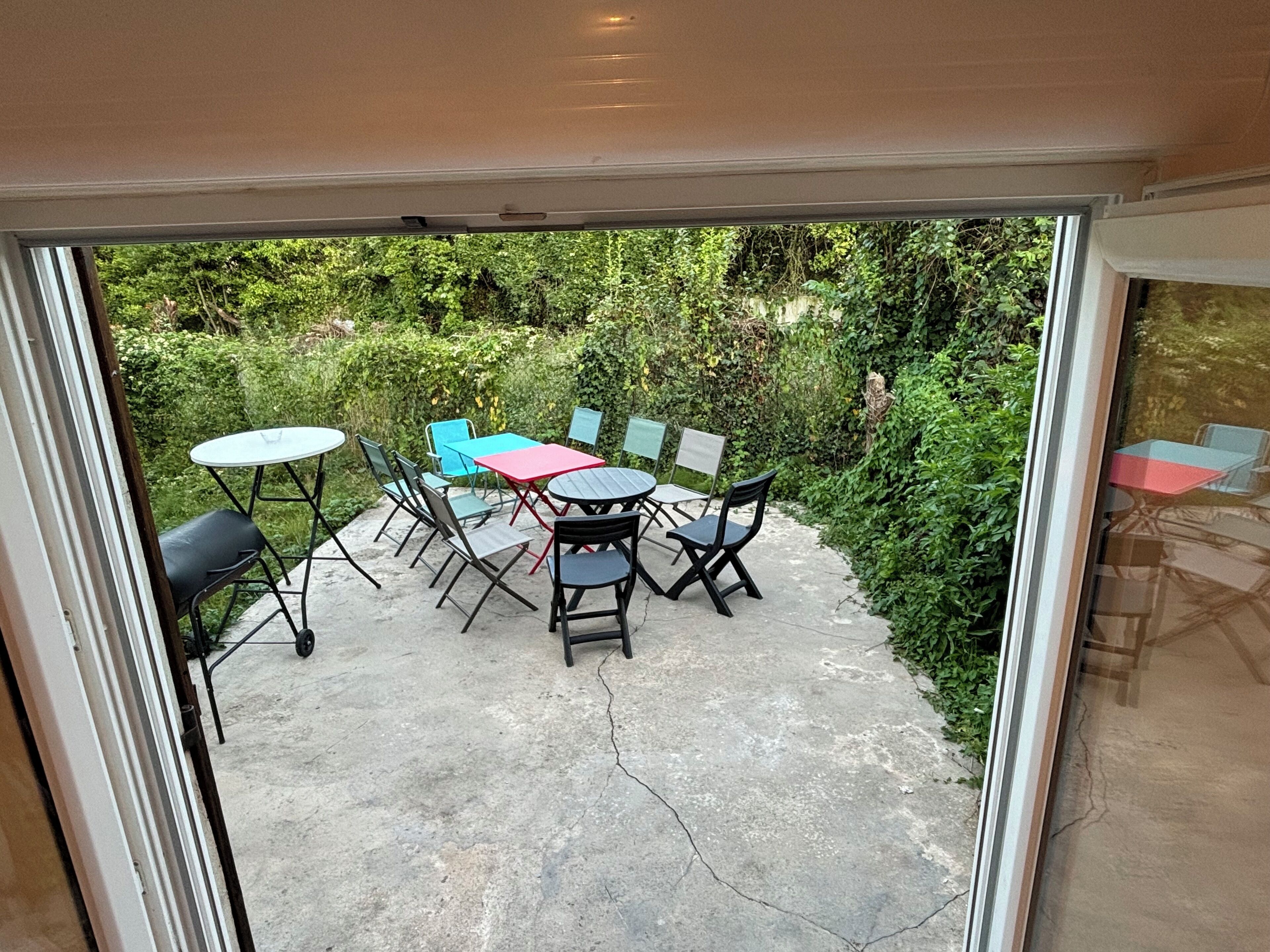 Eine Außenpatio mit Tisch und Stühlen, umgeben von viel Grün.