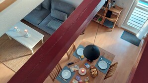 A dining area with a wooden table set for two, a sofa, and a staircase.