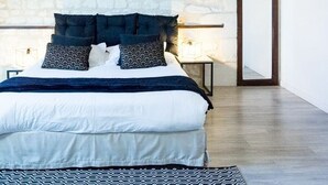 A bedroom with a stone wall, a bed with dark bedding, two wall clocks, and a mirror. - Quiet, comfortable TORIS B&B (Neuil)