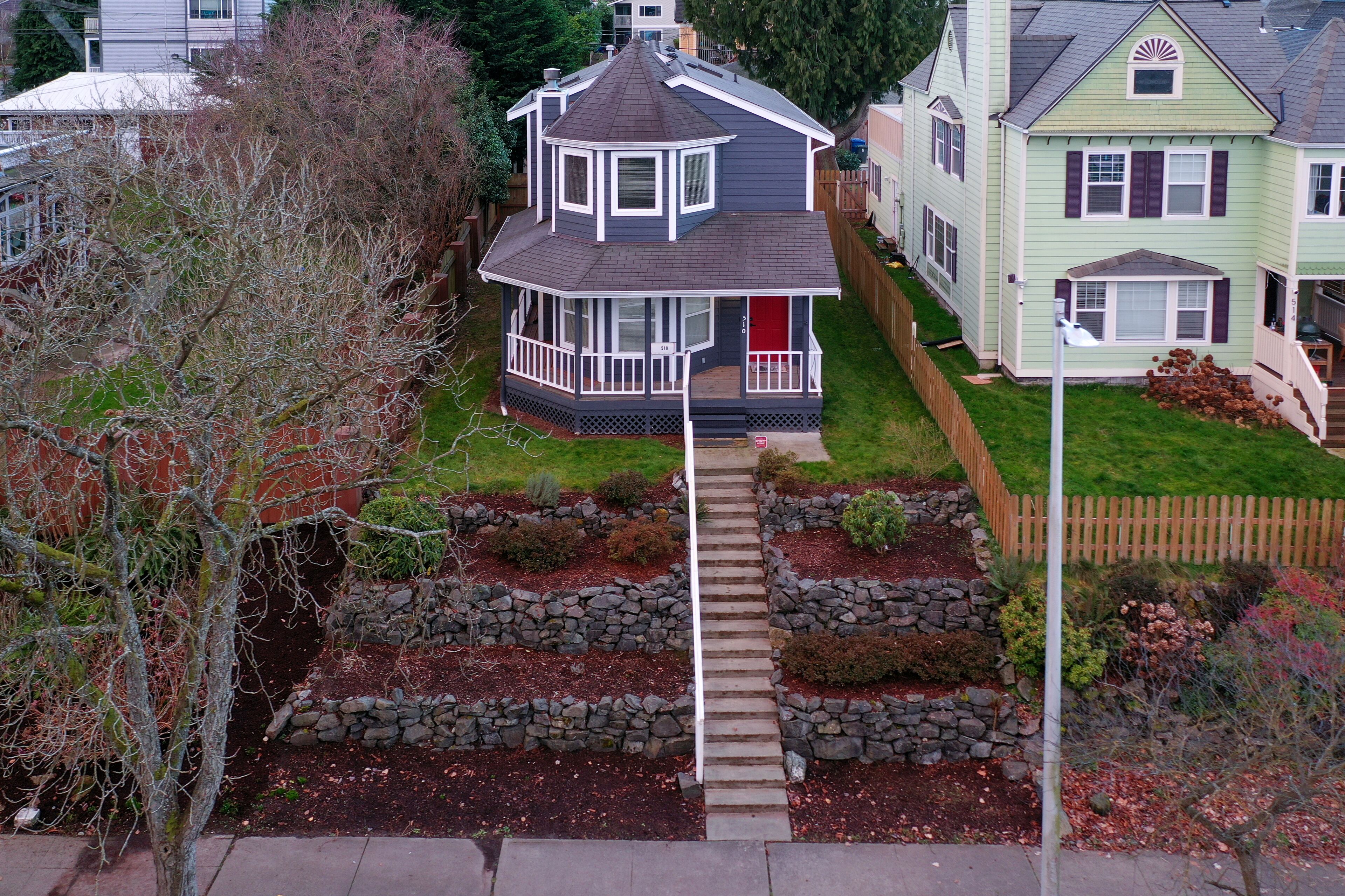 A two-story house with a wrap-around porch, a stone pathway leading to the front door, and a well-maintained garden with various plants and shrubs.