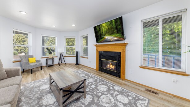 A modern living room with a fireplace, a flat-screen TV, and a large window with blinds.