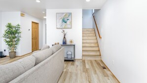 A modern living room with a sofa, a wooden staircase, and a potted plant.