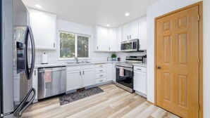 A modern kitchen with white cabinets, stainless steel appliances, and a wooden door.