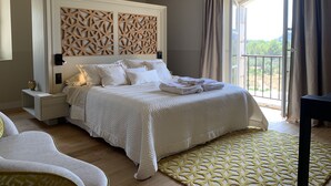 Une chambre spacieuse avec un grand lit, une tête de lit en bois, une table de chevet avec une lampe et une vue sur l’extérieur grâce à une porte coulissante.