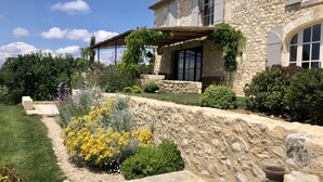 Un bâtiment en pierre doté d’un porche abrité, entouré de jardins bien entretenus et d’un mur en pierre.