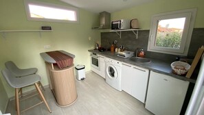 Cocina compacta con lavadora, microondas y lavabo. Hay dos sillas y un bote de basura.