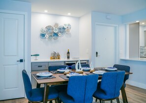 Un coin repas avec une table dressée pour quatre personnes, des chaises à l’assise bleue et des assiettes décoratives accrochées au mur.