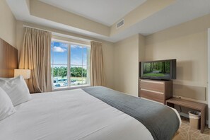A hotel room with a large bed, a television on a wooden stand, and a view of a parking lot and greenery outside. - Suite · The Point Lux Suite, close to Universal (Orlando)