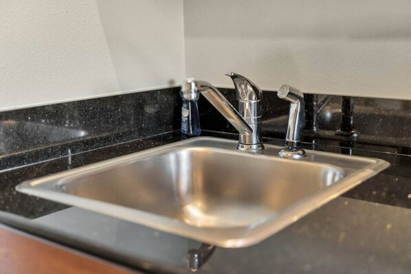 Lavello cucina in acciaio inossidabile con un moderno rubinetto, su un piano di lavoro nero e una parete bianca.