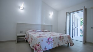 A bedroom with a bed, a nightstand, and a door leading to an outdoor area. - North Shell (Cala Gonone)