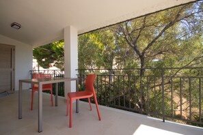 A balcony with a table and two chairs, overlooking a garden with trees and a fence. - North Shell (Cala Gonone)