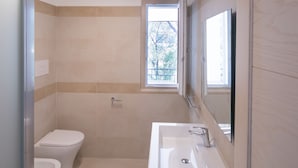 A modern bathroom with a toilet, sink, and shower. There is a window providing natural light and a mirror above the sink. - North Shell (Cala Gonone)