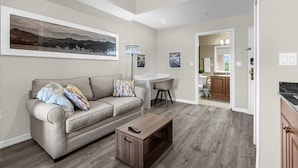 A spacious living room with a sofa, coffee table, and a dining area. A kitchen is visible in the background. - Studio · The point Studio 10 min Universal (Orlando)
