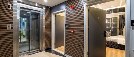 Un moderno vestíbulo de hotel con un ascensor de vidrio, un panel de pared de madera y un cartel que indica la habitación 302.