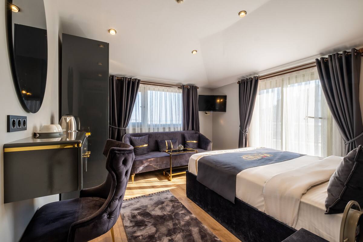 A modern hotel room with a bed, a sofa, a desk, and a TV.