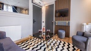 Un salon moderne avec une table basse en verre, un canapé gris, un tapis à motifs et un téléviseur fixé sur un mur en panneaux de bois.