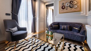 A modern living room with a dark armchair, a dark sofa with gold accents, a glass coffee table, and a black and white rug. - Wind Suit (Istanbul)