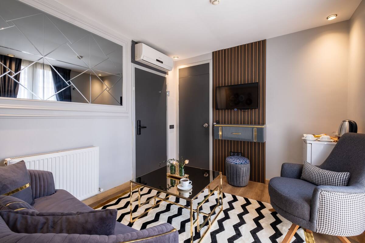 A modern living room with a sofa, a coffee table, a TV mounted on the wall, and a patterned rug.