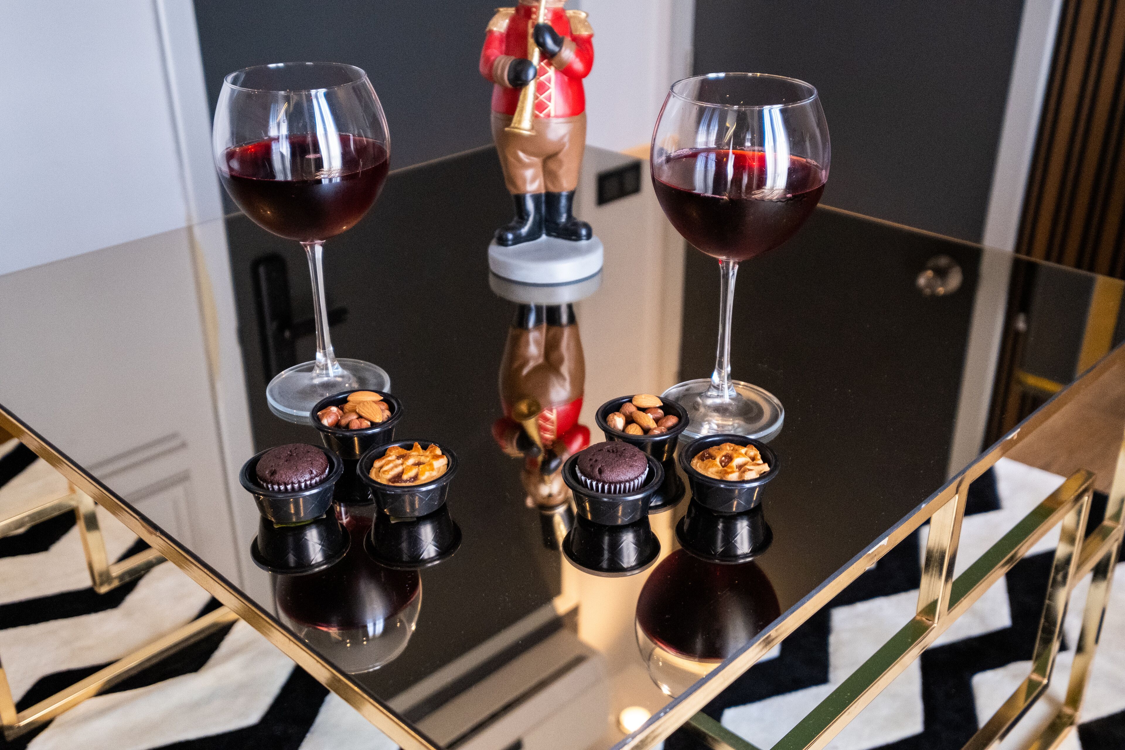 A glass table with two wine glasses, a nutcracker figurine, and several small containers with nuts and chocolate.