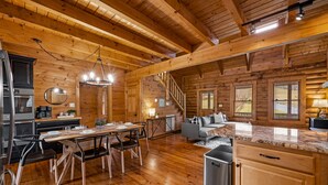 Una cabaña de troncos espaciosa con interior de madera, un comedor con mesa y sillas, una cocina con electrodomésticos modernos y una sala de estar acogedora con sofá y chimenea.