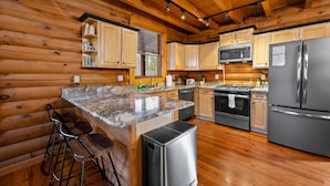 A log cabin kitchen with wooden walls, granite countertops, stainless steel appliances, and a bar area with stools.